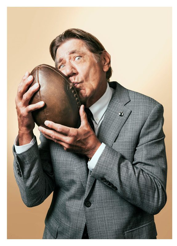 An old man wearing gray suit, holding a leather football